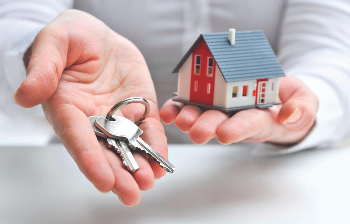 Hands cupping a set of keys beside a small red-and-white house model, symbolizing home purchase or real estate access