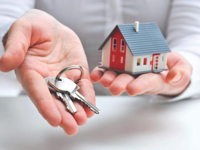 Hands cupping a set of keys beside a small red-and-white house model, symbolizing home purchase or real estate access