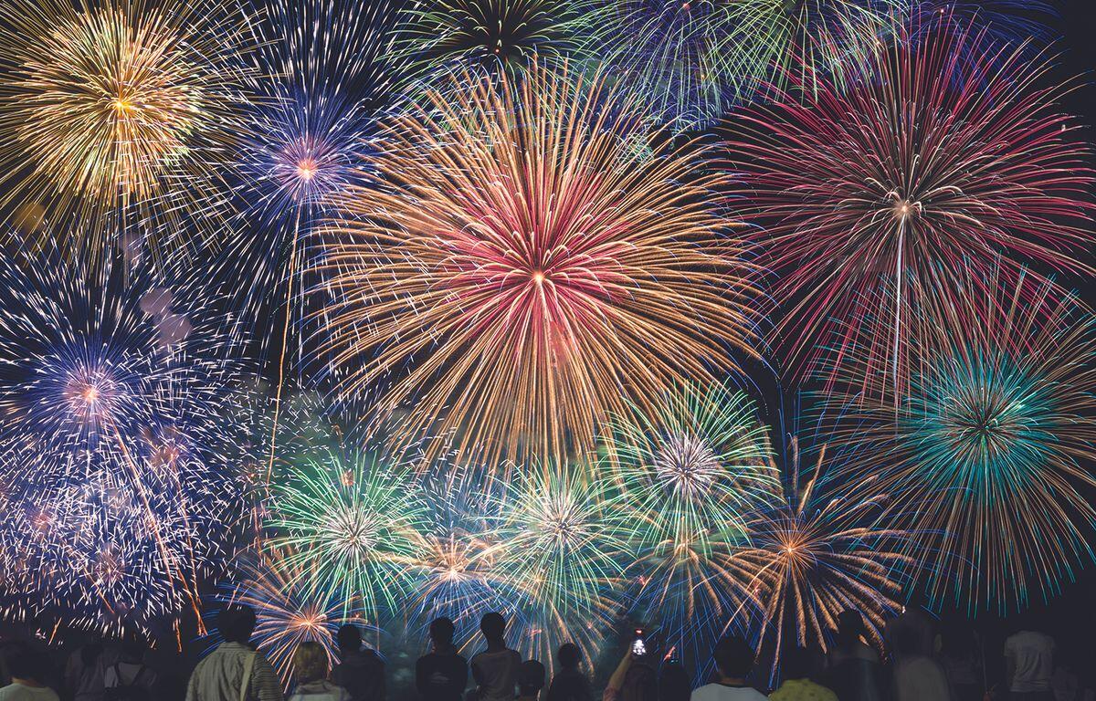Colorful fireworks explode in the night sky above a crowd of silhouetted spectators observing the display.