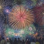 Colorful fireworks explode in the night sky above a crowd of silhouetted spectators observing the display.