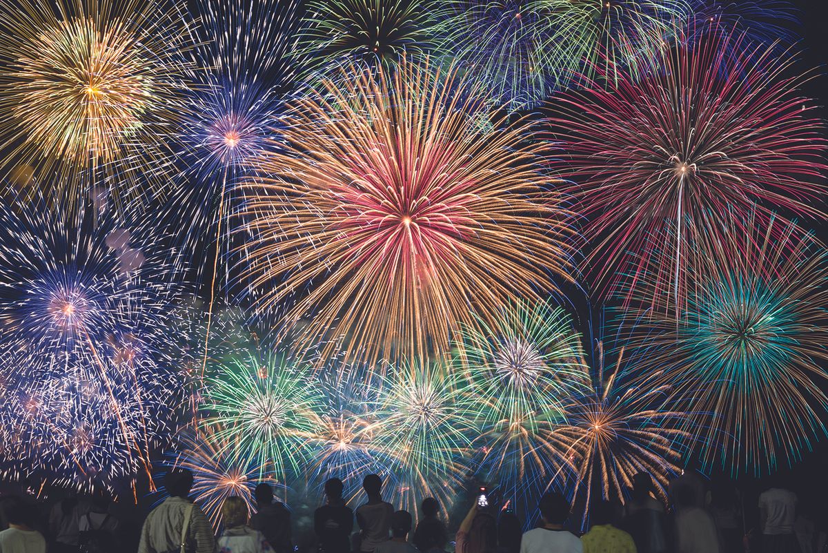 Colorful fireworks explode in the night sky above a crowd of silhouetted spectators observing the display.
