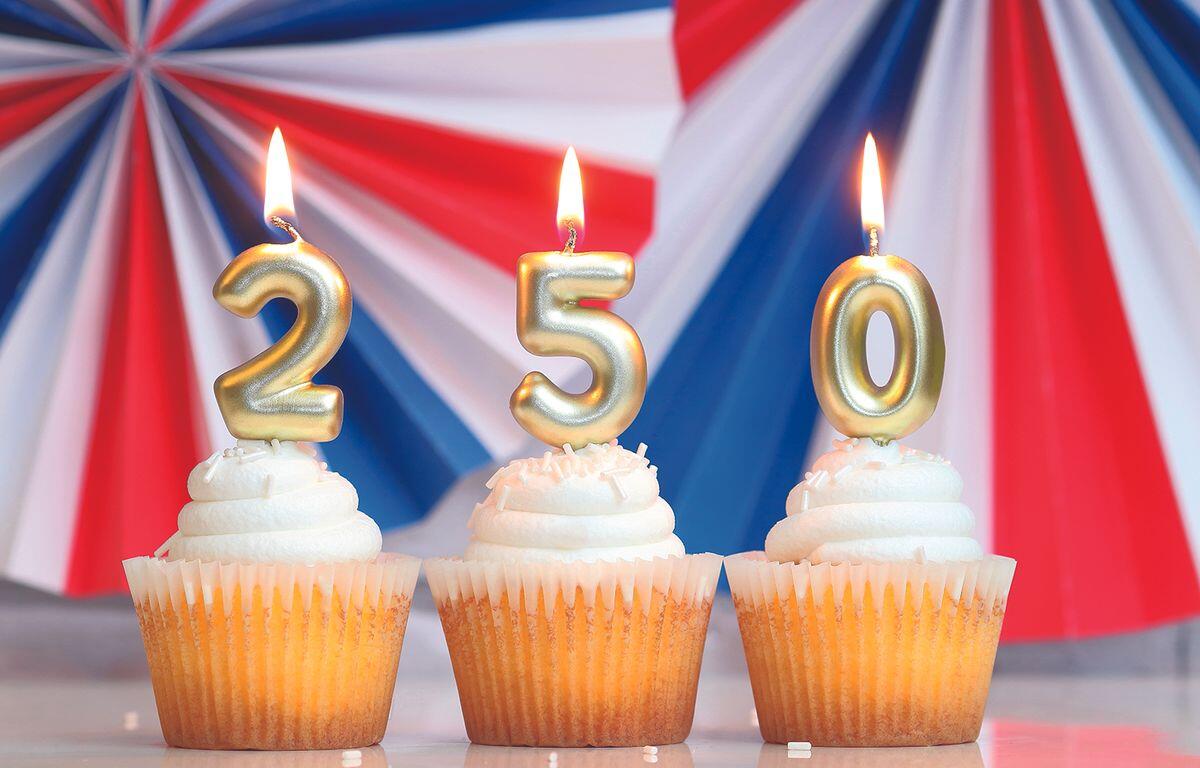 Three cupcakes with gold numeral candles 2, 5, and 0 against a patriotic red‑white‑blue backdrop.