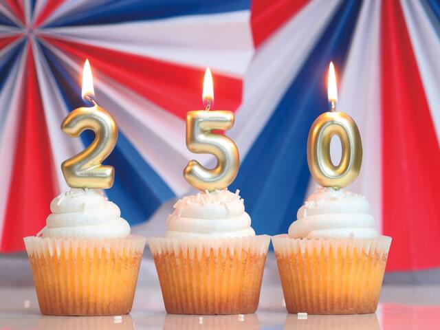 Three cupcakes with gold numeral candles 2, 5, and 0 against a patriotic red‑white‑blue backdrop.