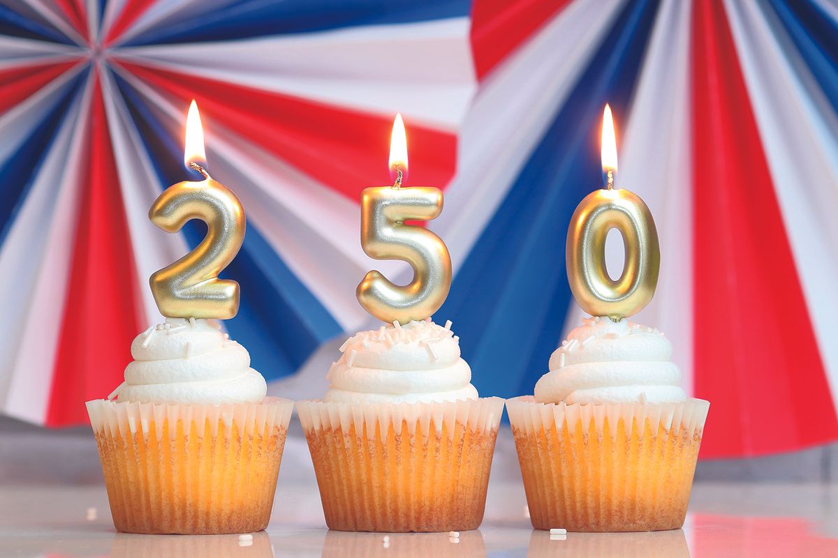 Three cupcakes with gold numeral candles 2, 5, and 0 against a patriotic red‑white‑blue backdrop.