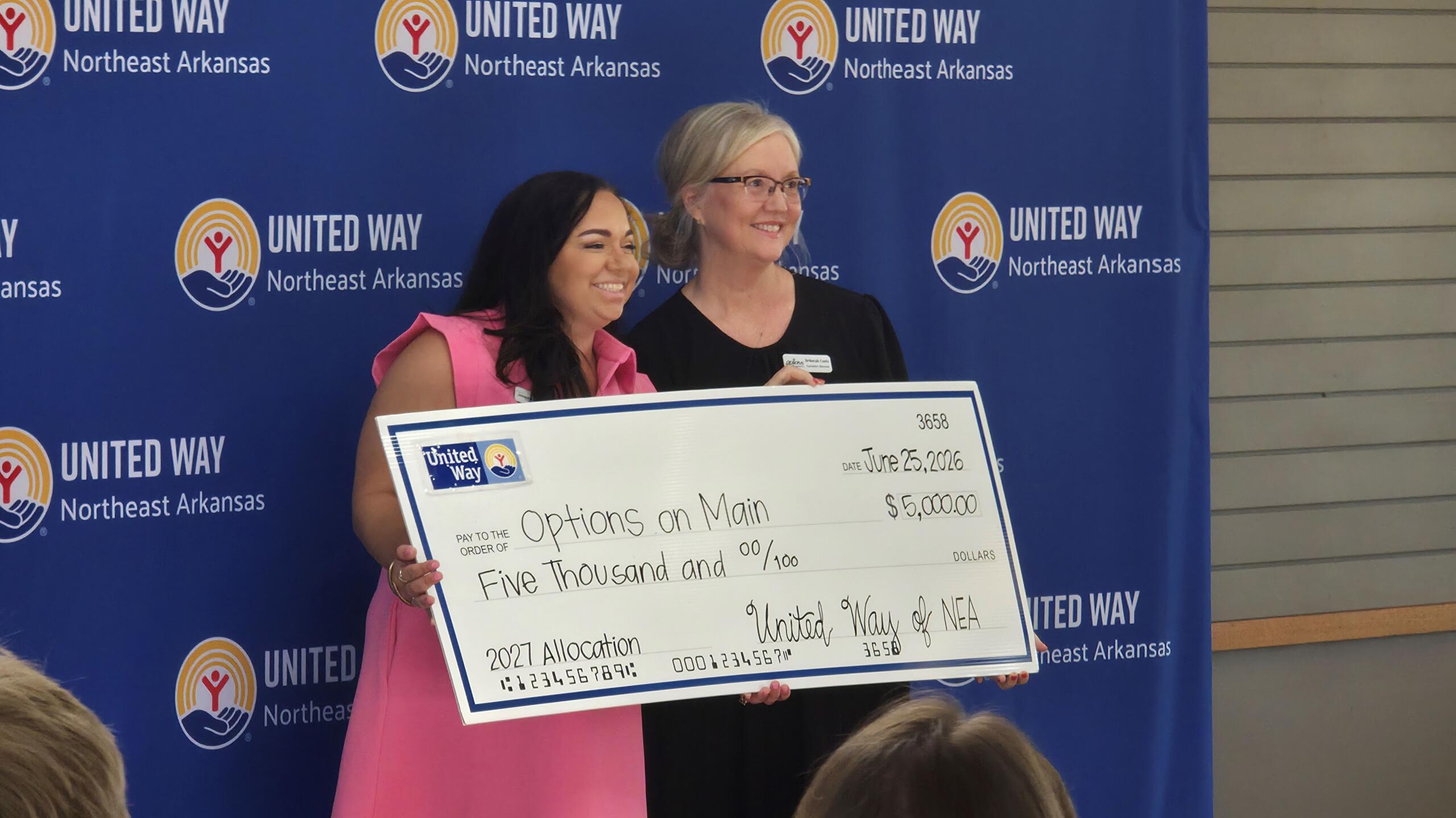 Two women standing in front of a United Way backdrop, holding a large ceremonial check for $5,000 dated June 25, 2026.
