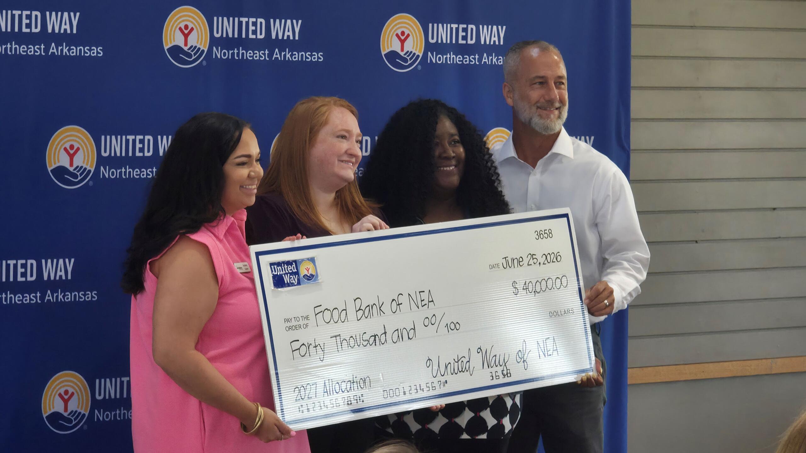 Group of four people posing with a large ceremonial check against a blue United Way backdrop.