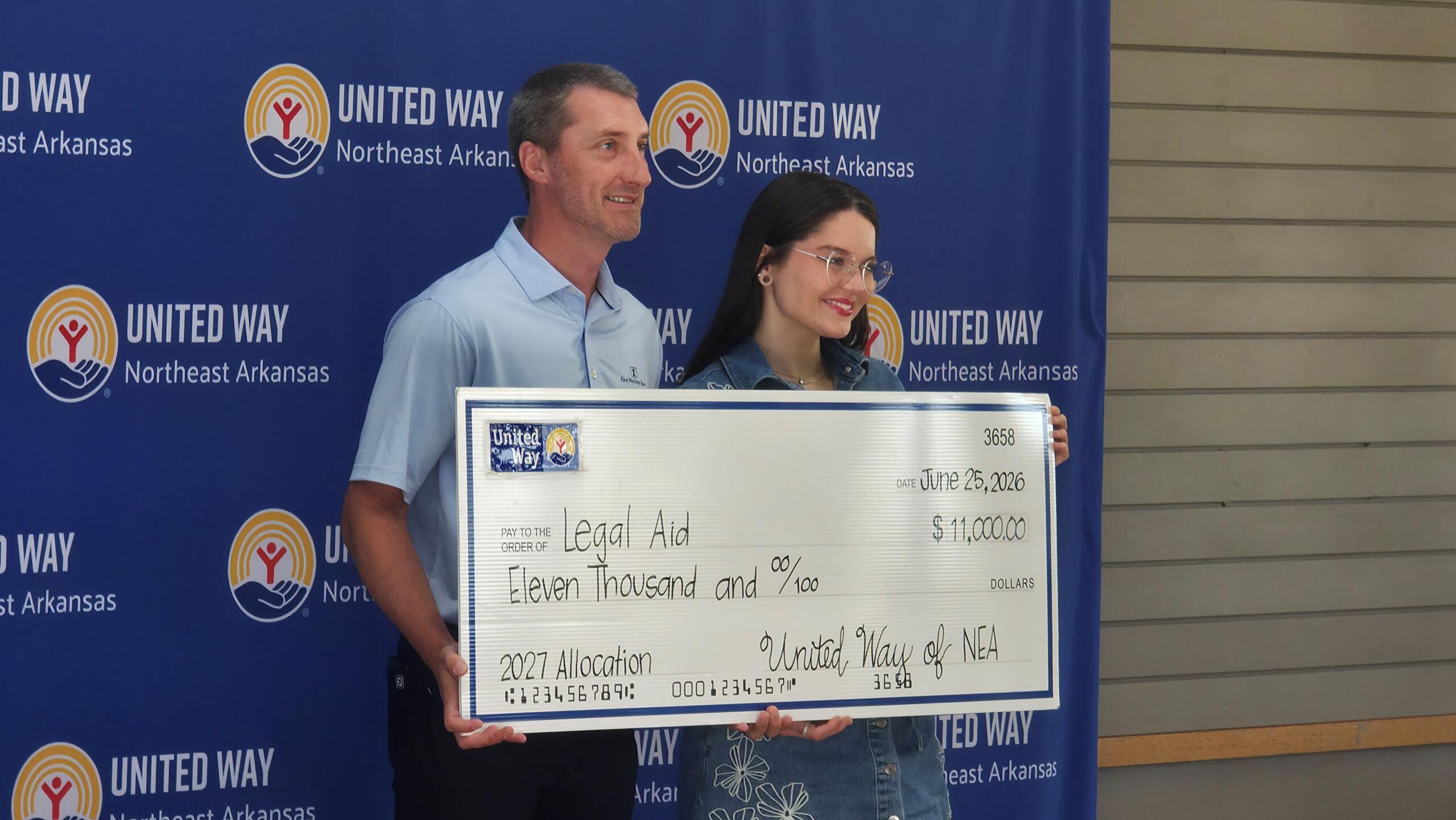 Two adults pose with a large ceremonial check in front of a United Way backdrop for Northeast Arkansas, smiling at the camera.