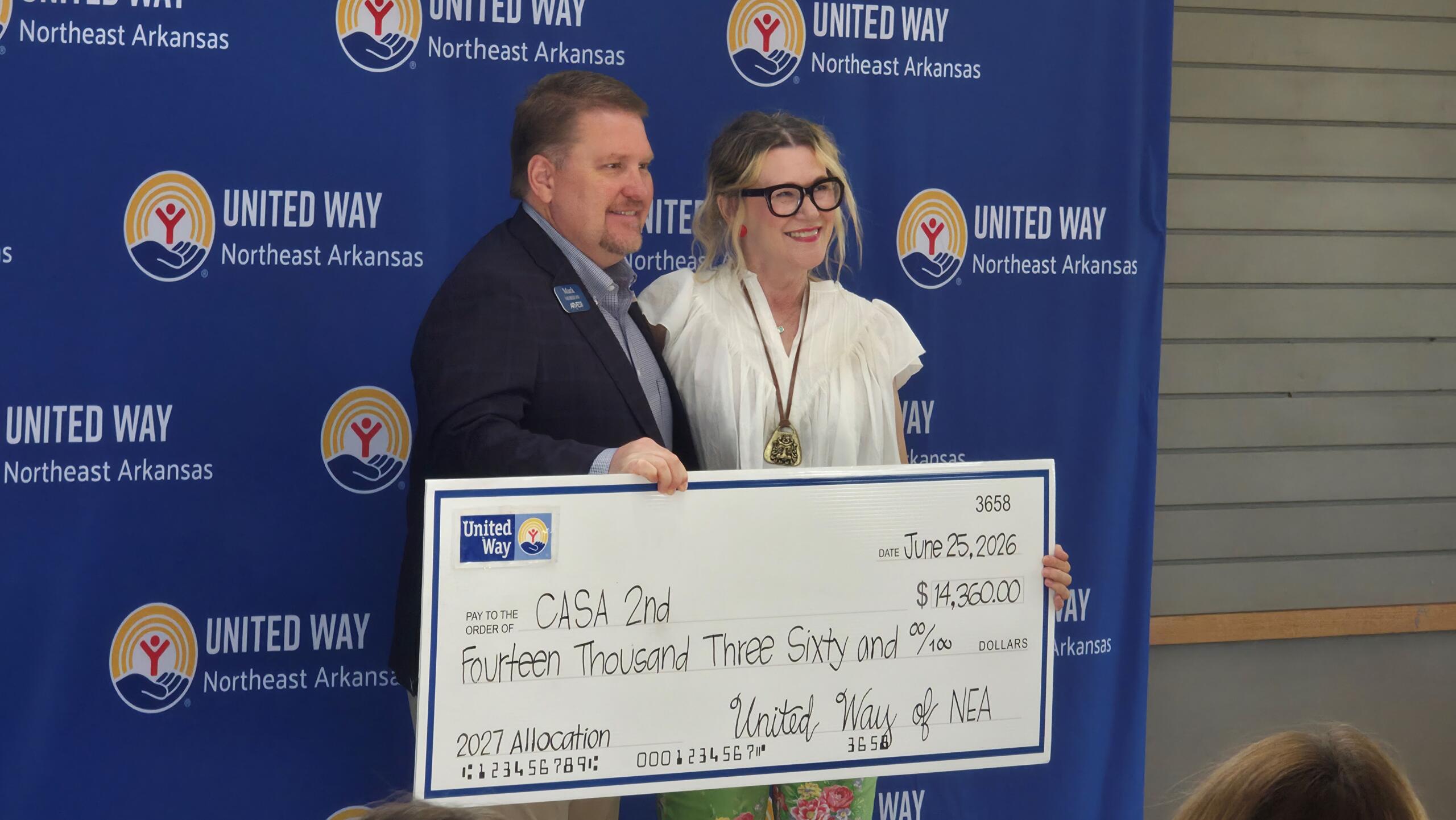 Two adults smile as they hold a large ceremonial check in front of a United Way banner for Northeast Arkansas Shipping the presentation event
