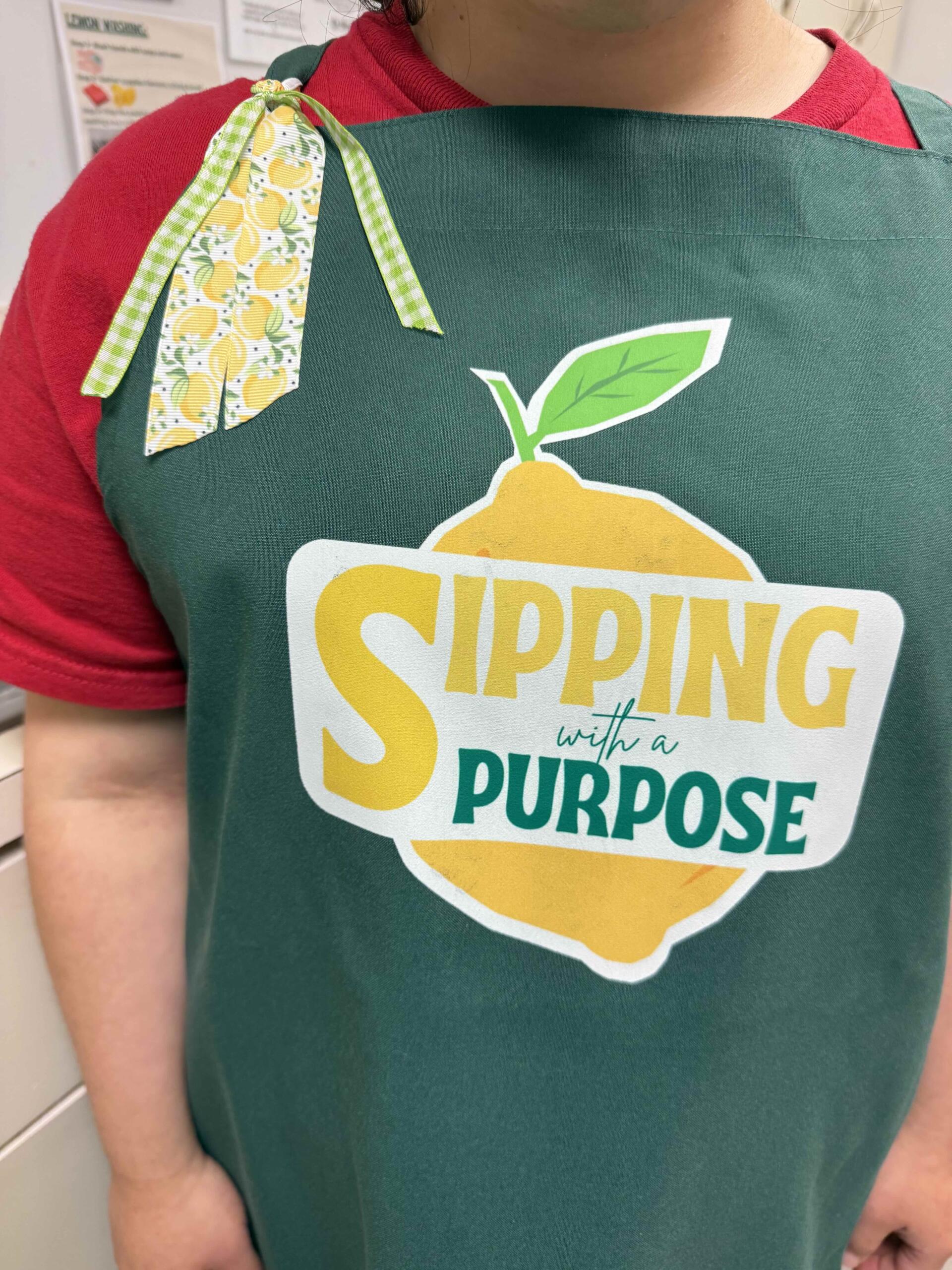 Person wearing a green apron with a lemon graphic and the text 'SPRING with a PURPOSE' over a red shirt.