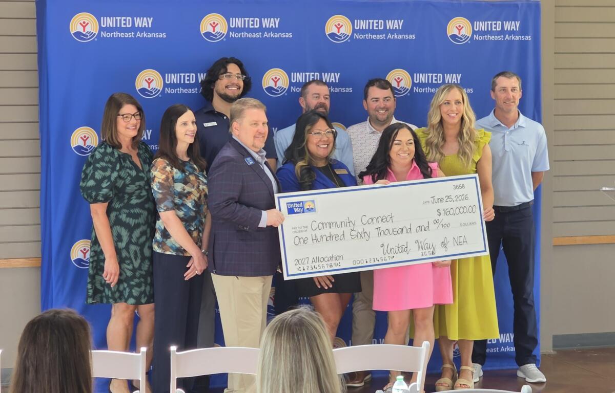 Group of ten adults posing with a large ceremonial check in front of a United Way Northeast Arkansas backdrop, smiling at the camera.