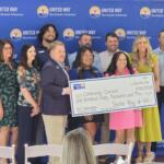 Group of ten adults posing with a large ceremonial check in front of a United Way Northeast Arkansas backdrop, smiling at the camera.