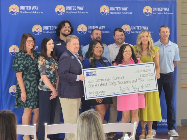 Group of ten adults posing with a large ceremonial check in front of a United Way Northeast Arkansas backdrop, smiling at the camera.