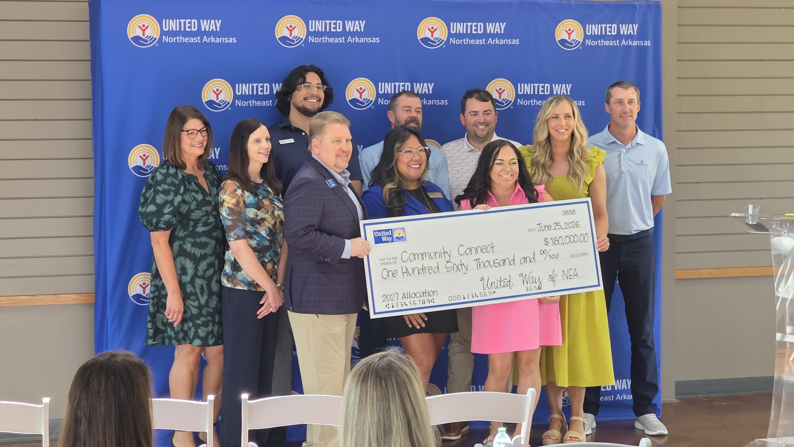 Group of ten adults posing with a large ceremonial check in front of a United Way Northeast Arkansas backdrop, smiling at the camera.