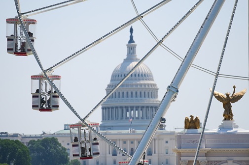 Ferris wheel with red cabins in the foreground and the U.S. Capitol building in Washington, D.C., in the background.