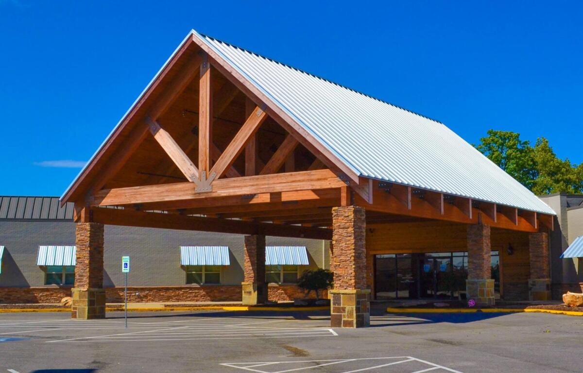 Commercial building with a wooden portico and a silver metal gabled roof under a bright blue sky in a shopping plaza.