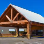 Commercial building with a wooden portico and a silver metal gabled roof under a bright blue sky in a shopping plaza.