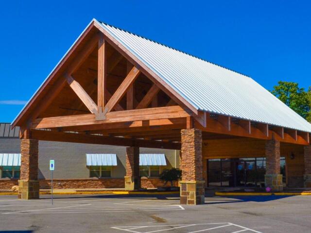 Commercial building with a wooden portico and a silver metal gabled roof under a bright blue sky in a shopping plaza.