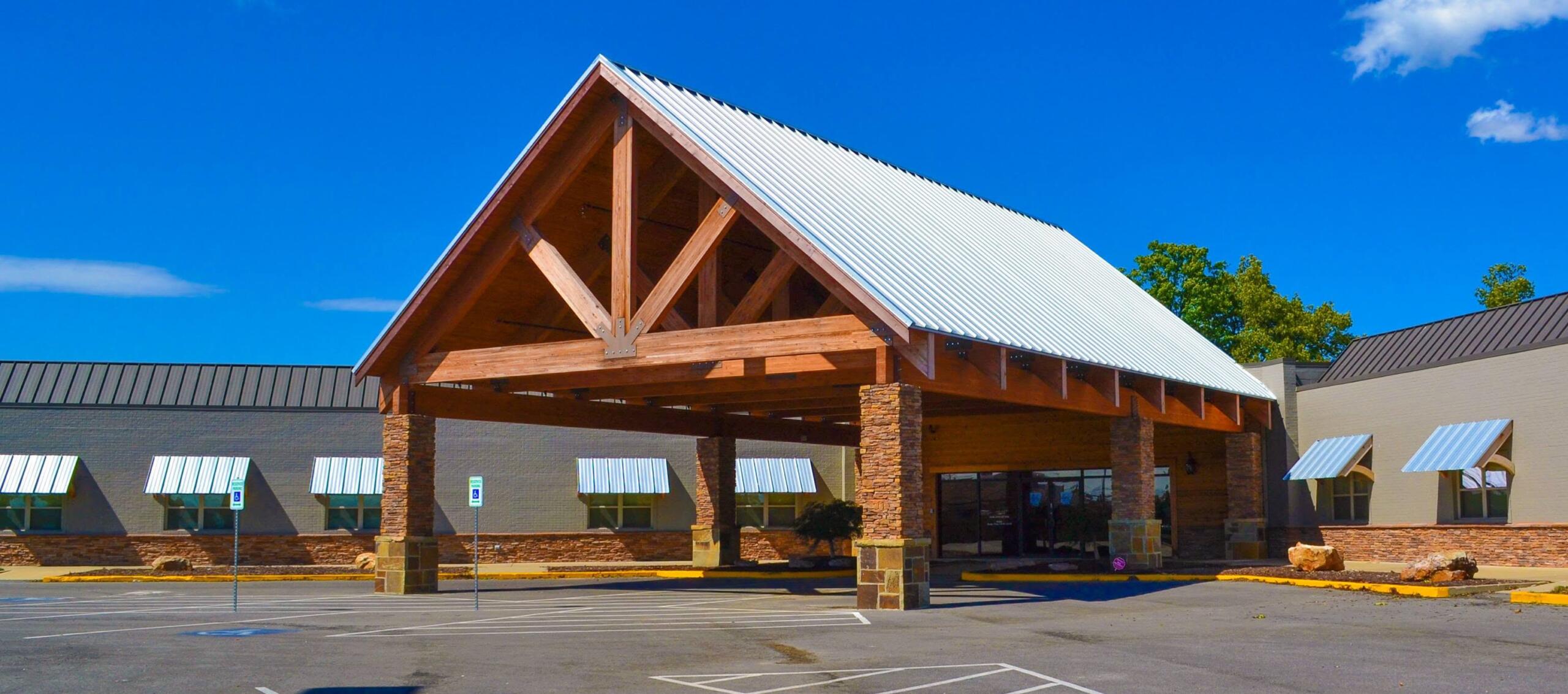 Commercial building with a wooden portico and a silver metal gabled roof under a bright blue sky in a shopping plaza.