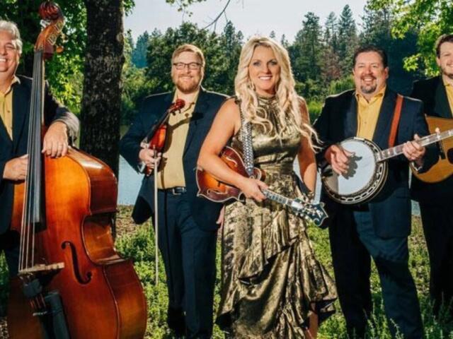 Five-member band outdoors: a woman in a metallic gold dress holding a violin, flanked by four men with a upright bass, violin, banjo, and guitar.