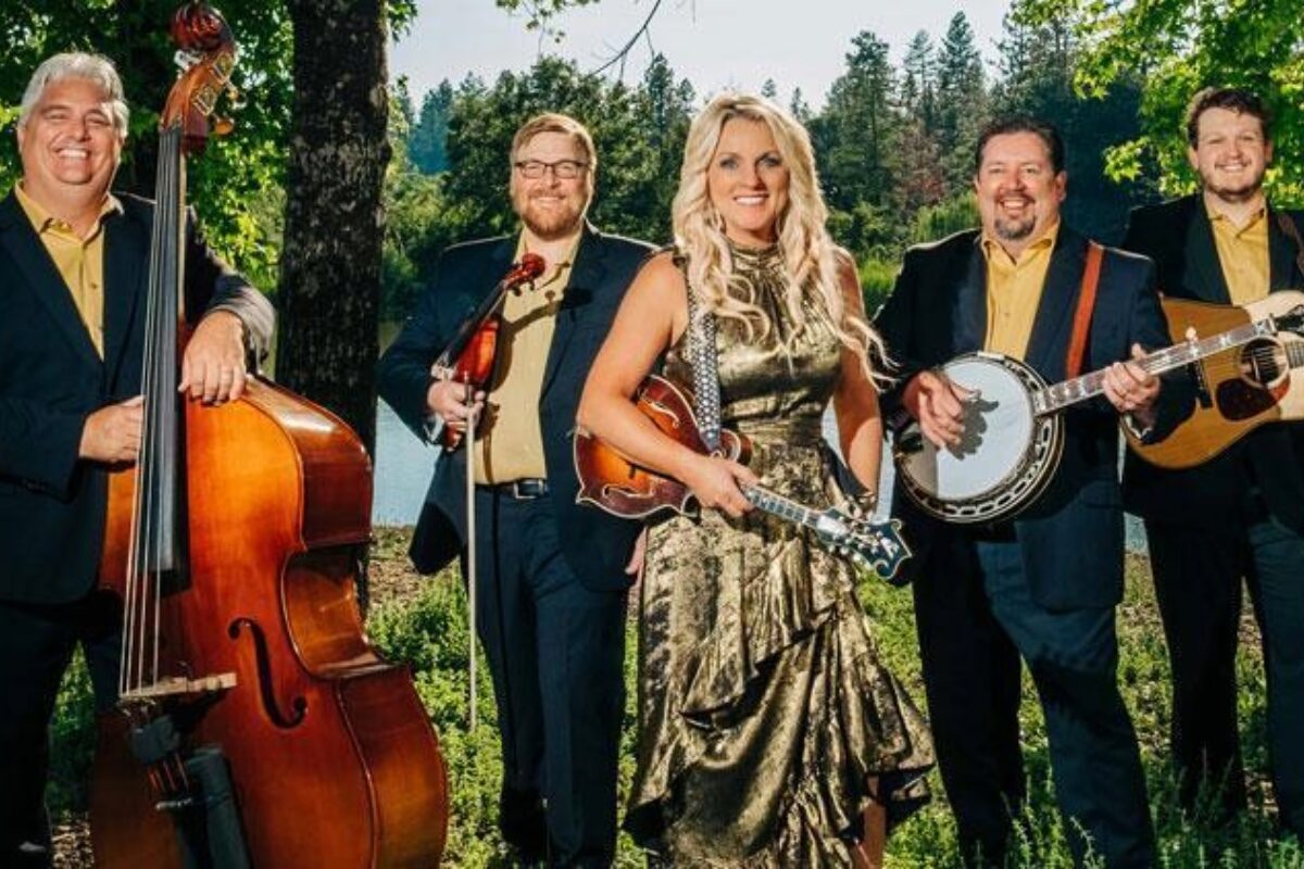 Five-member band outdoors: a woman in a metallic gold dress holding a violin, flanked by four men with a upright bass, violin, banjo, and guitar.