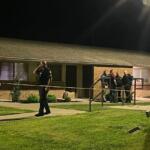 Police officers stand behind yellow caution tape outside a brick apartment building at night, investigating.