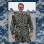 Male U.S. Navy service member in camouflage uniform standing on an airfield with jets in the background, name tag McDonald visible.