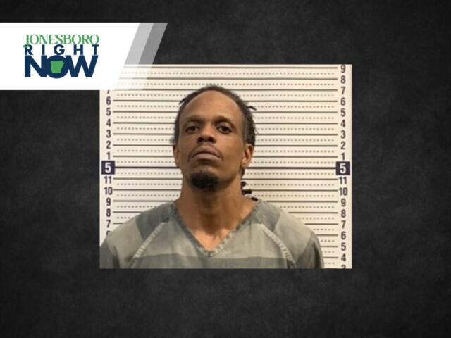 Mugshot of a man in a gray inmate jumpsuit standing before a height chart, with Jonesboro Now logo in the top-left corner.