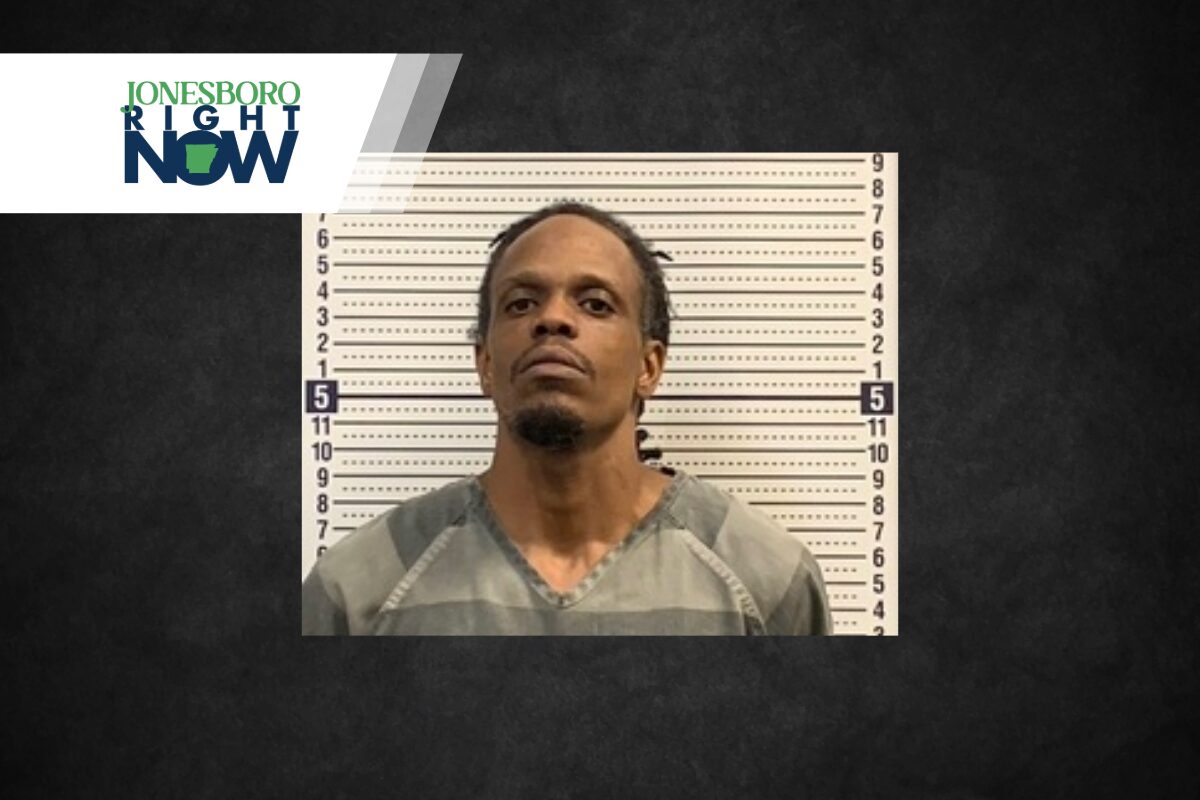 Mugshot of a man in a gray inmate jumpsuit standing before a height chart, with Jonesboro Now logo in the top-left corner.