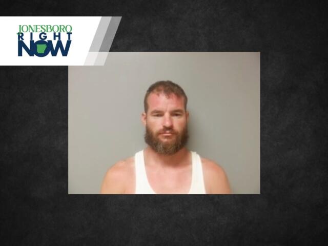 Mugshot-style photo of a bearded man in a white tank top, standing against a plain grey wall, with a Jonesboro Right Now logo in the top-left corner.