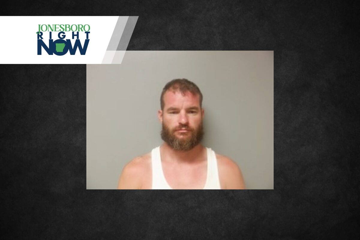 Mugshot-style photo of a bearded man in a white tank top, standing against a plain grey wall, with a Jonesboro Right Now logo in the top-left corner.
