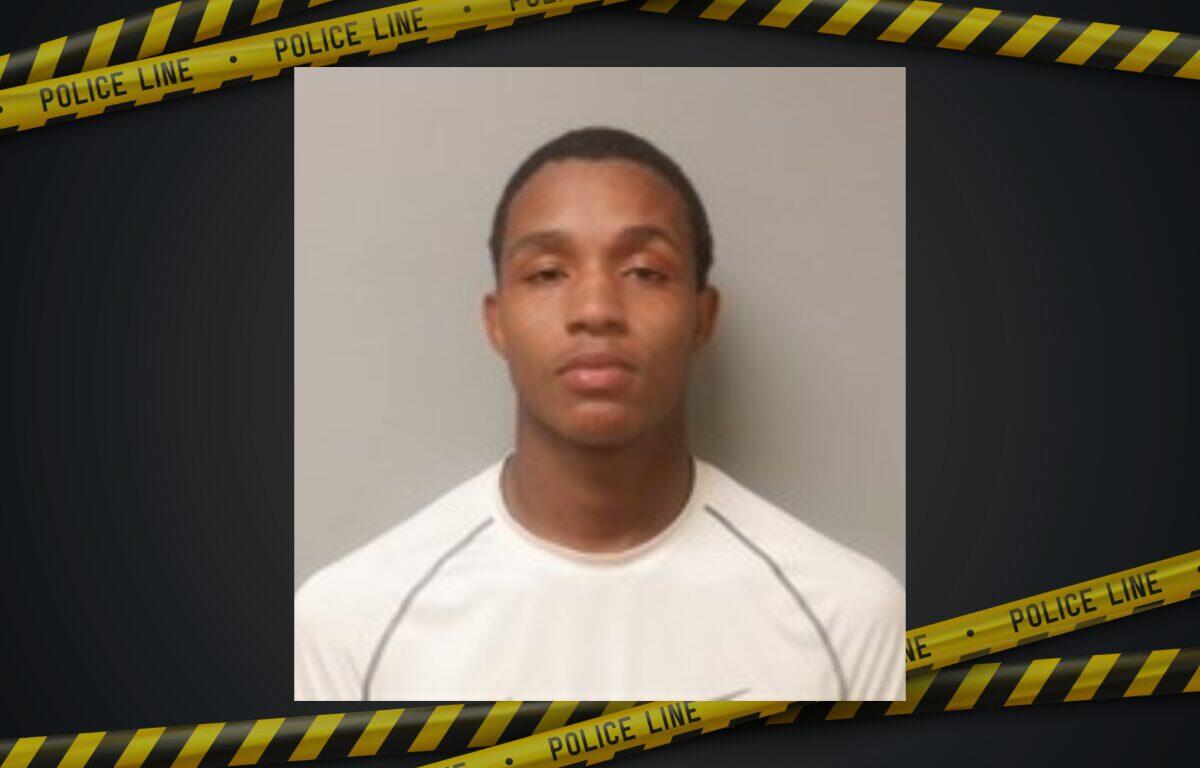 Mugshot of a young man with short hair wearing a white shirt, neutral expression, gray wall background, police tape border framing the image.