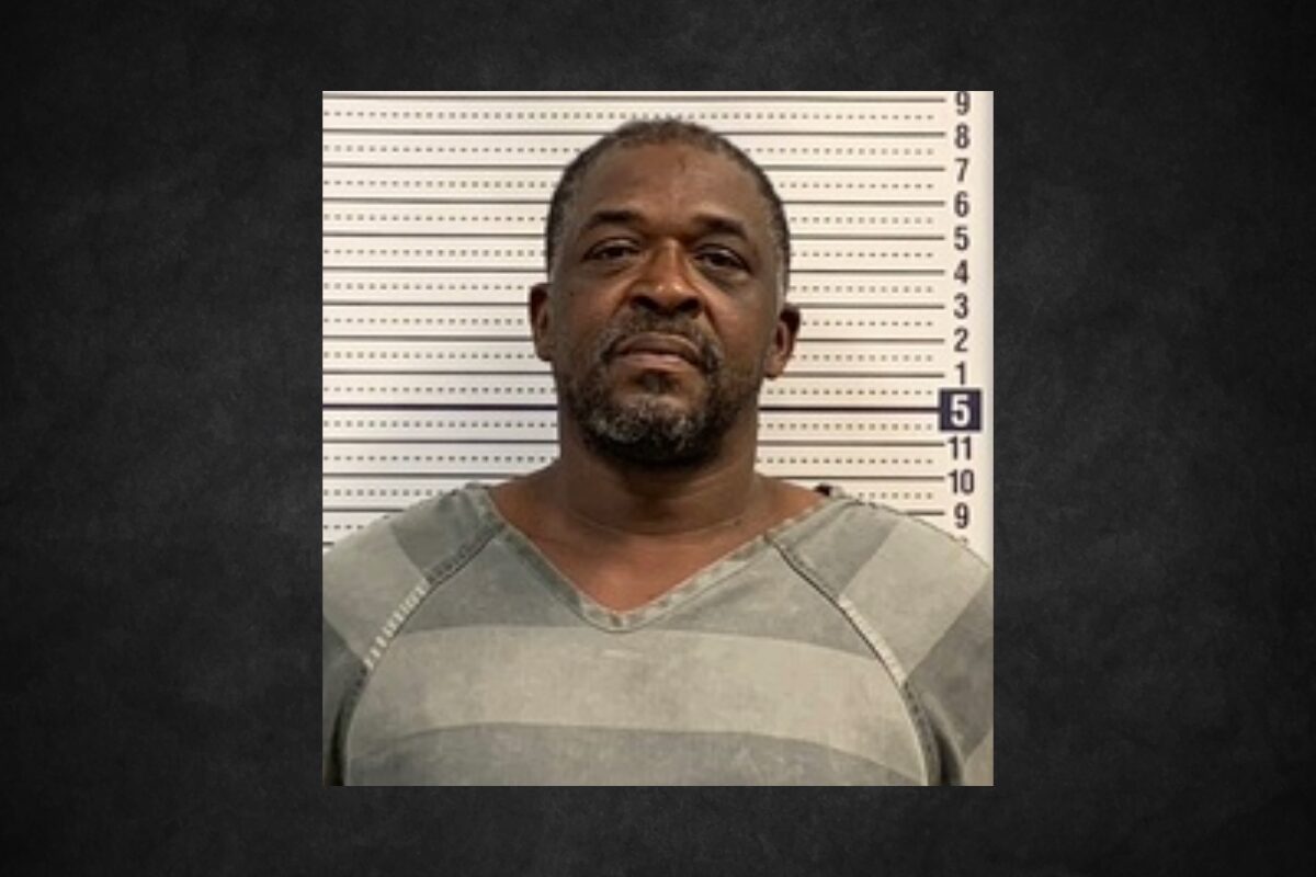 Mugshot of a middle-aged man in a gray striped jail uniform, standing against a height chart behind him.