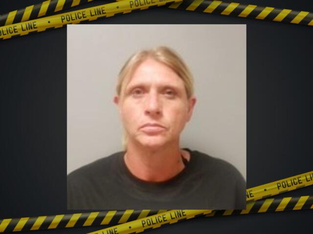 Mugshot of a blonde woman in a dark shirt, neutral expression, against a plain background with police tape framing the image.