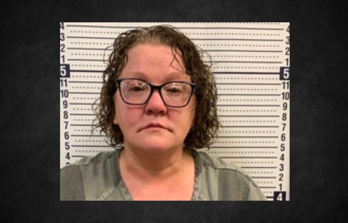 Mugshot of a middle-aged woman with glasses in a gray top, standing before a height-measure backdrop.