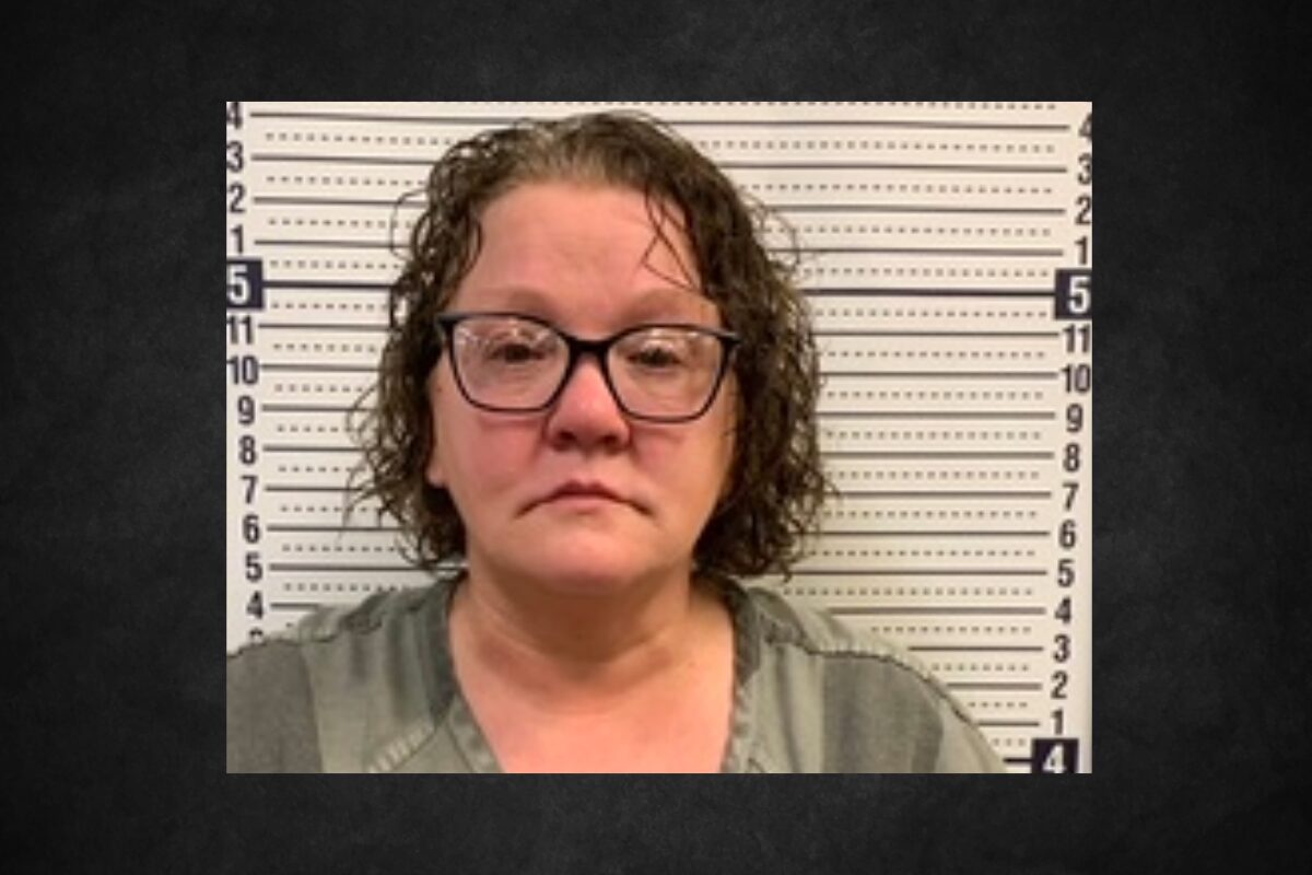 Mugshot of a middle-aged woman with glasses in a gray top, standing before a height-measure backdrop.