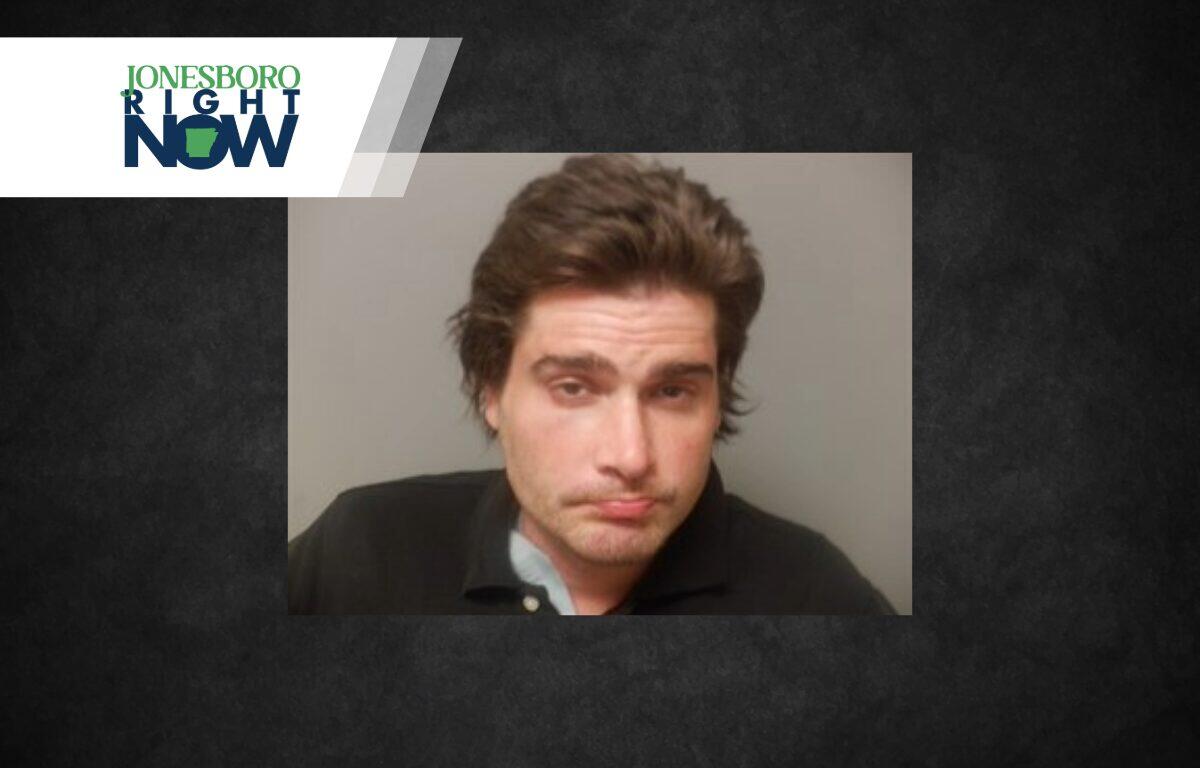 Mugshot-style photo of a disheveled man with brown hair wearing a dark polo, on a gray background, with a Jonesboro Right Now logo in the top-left corner.