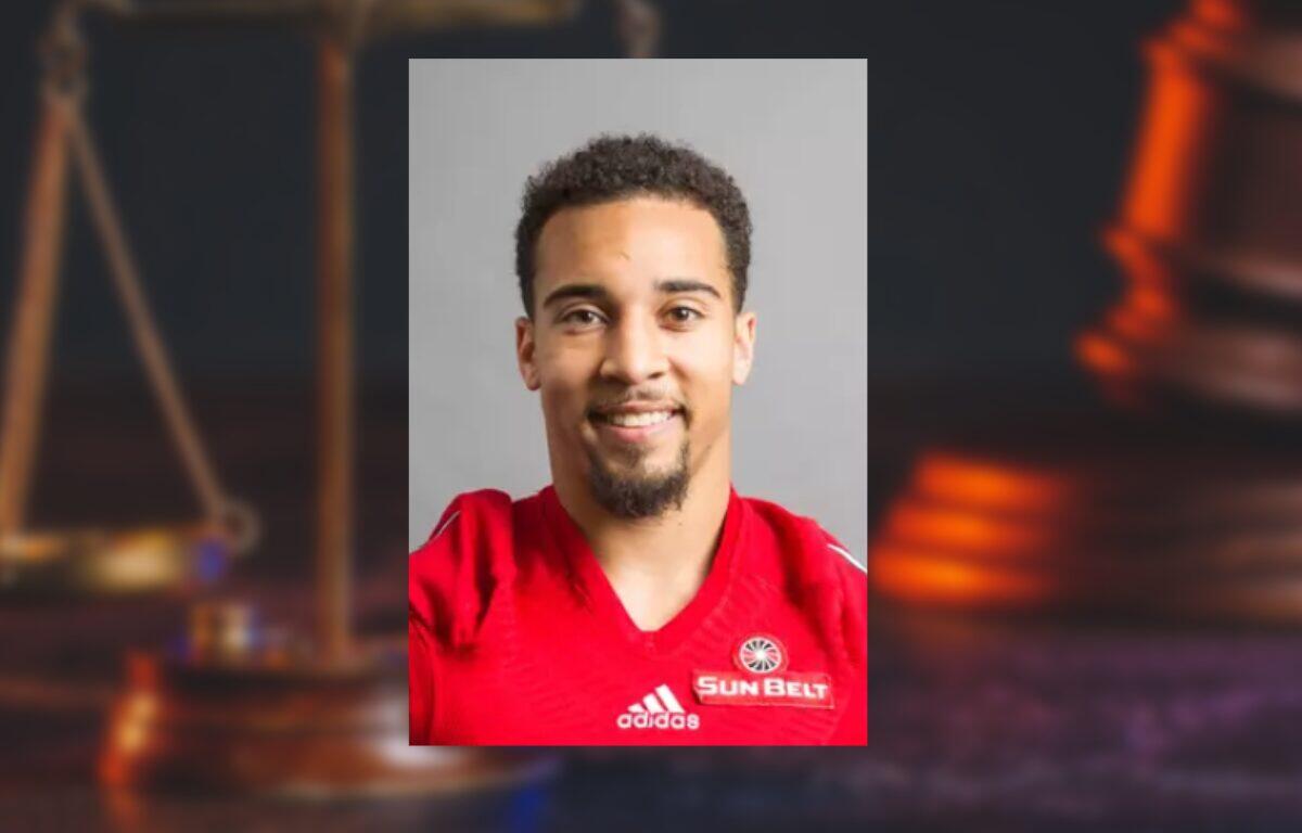 Portrait of a smiling man in a red Adidas jersey with a Sun Belt badge against a neutral gray background (informative athletic headshot).