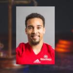 Portrait of a smiling man in a red Adidas jersey with a Sun Belt badge against a neutral gray background (informative athletic headshot).