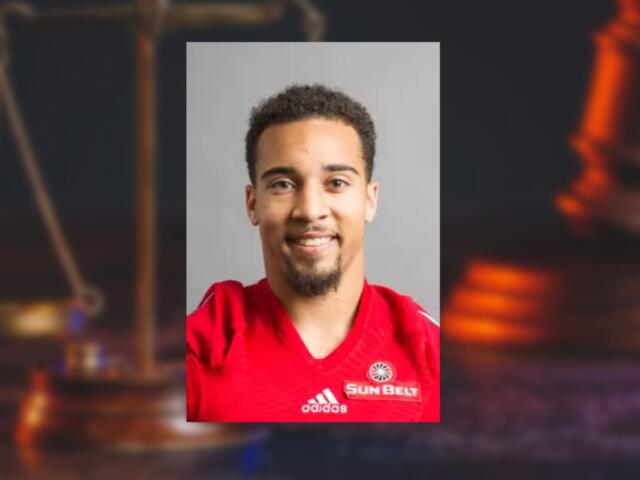 Portrait of a smiling man in a red Adidas jersey with a Sun Belt badge against a neutral gray background (informative athletic headshot).