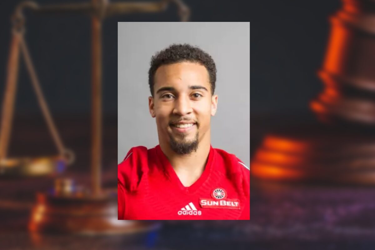 Portrait of a smiling man in a red Adidas jersey with a Sun Belt badge against a neutral gray background (informative athletic headshot).