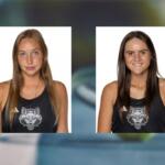 Two young women in black tank tops with a wolf logo, white background; left: light brown hair, neutral expression, right: dark brown hair, smiling.