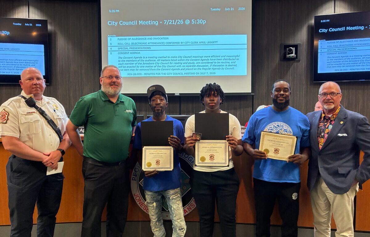 Six people stand behind a council desk; four award recipients hold certificates, flanked by officials during City Council meeting.
