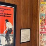 Framed vintage posters on wood panels, one red text poster depicting a bullfight scene and a Western-themed poster to the right