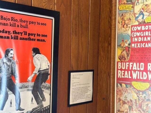 Framed vintage posters on wood panels, one red text poster depicting a bullfight scene and a Western-themed poster to the right