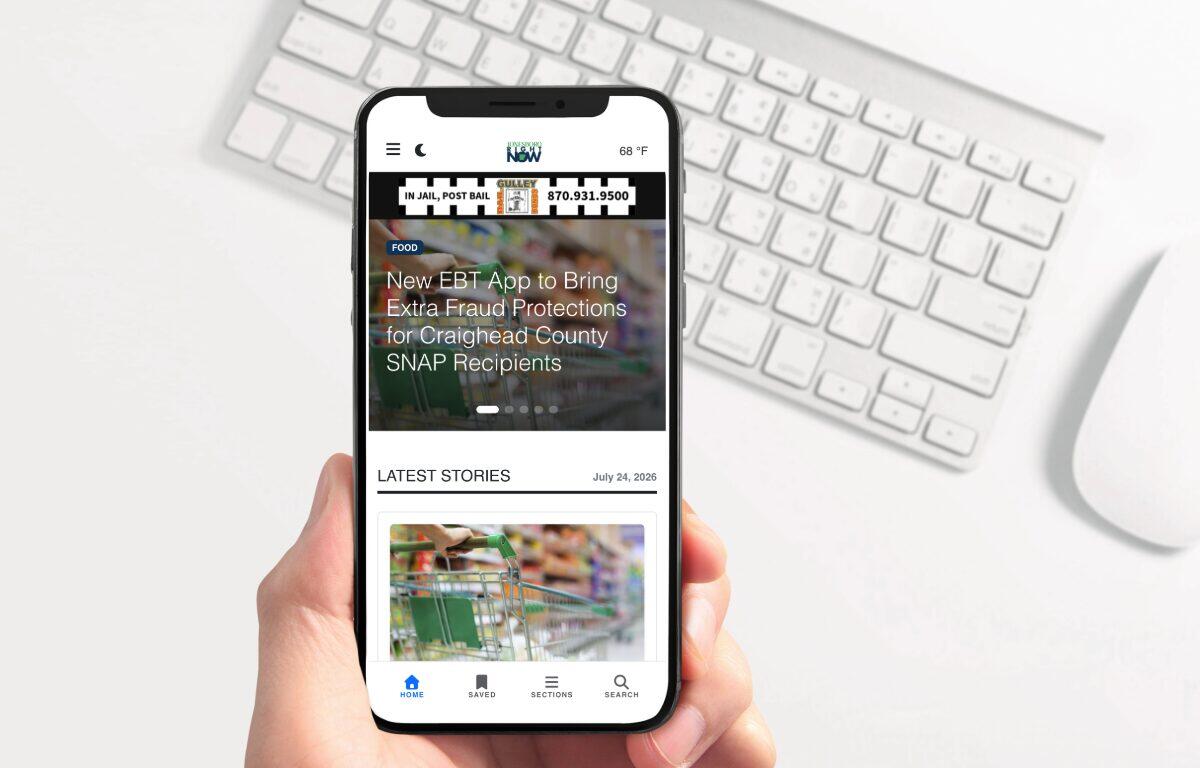 Handheld smartphone displaying a mobile news app with a headline about EBT fraud protections and a 'Latest Stories' section.