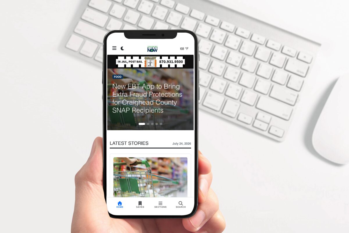 Handheld smartphone displaying a mobile news app with a headline about EBT fraud protections and a 'Latest Stories' section.