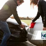 Two people inspect the front ends of two cars after a collision, with a news logo overlay in the corner.