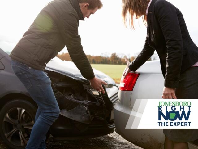 Two people inspect the front ends of two cars after a collision, with a news logo overlay in the corner.