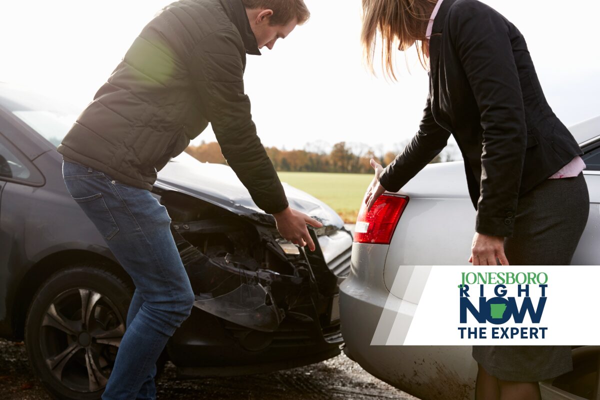 Two people inspect the front ends of two cars after a collision, with a news logo overlay in the corner.