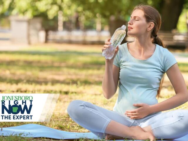 Pregnant or exercises woman sitting cross‑legged on a yoga mat in a park, sipping water with eyes closed; Jonesboro Right Now logo in the lower left corner.